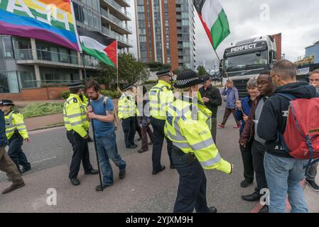 London, UK. 5th September 2017. Police force the people walking slowly with flags in front of a lorry going towards the West gate into the world's largest arms fair held in London's docklands off the road. This was part of the 'No Faith in War' day of protests organised by various faith groups. Before I arrived there had been a lock-in on the approach road stopping deliveries coming to set up the fair through the East gate. This was followed by a Quaker meeting at the side of the road during which a number of people stood or sat to block the road and several who refused to move were arrested. Stock Photo