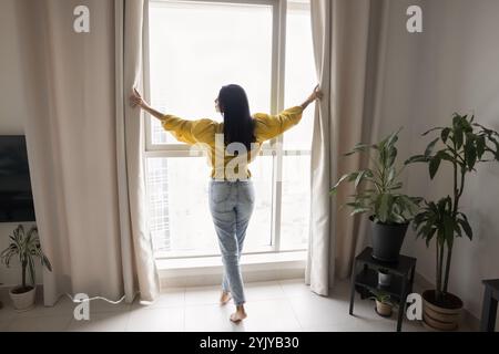 Beautiful black haired young woman standing at large window Stock Photo