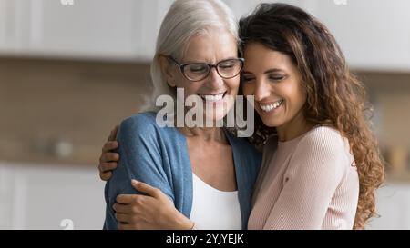 Two multigenerational women standing indoor and cuddling tightly Stock Photo