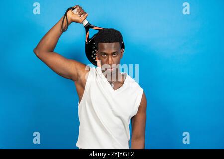 Young black man wearing white shirt holding beach tennis racket on vibrant blue background Stock Photo