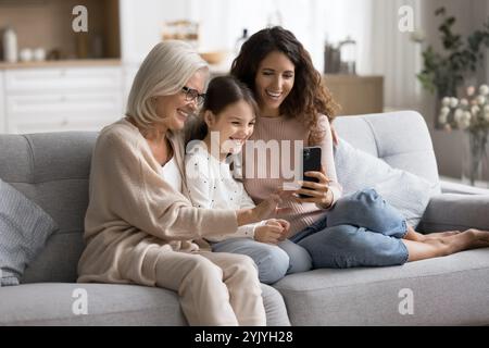 Three women, kid, granny and adult female using smartphone together Stock Photo