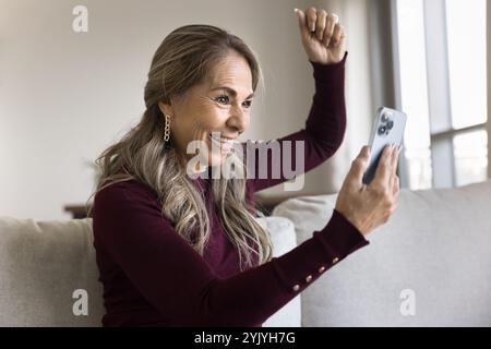 Happy overjoyed retired Latin woman holding smartphone Stock Photo