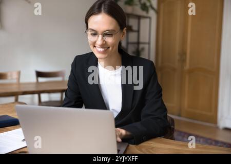 Young woman working on laptop is seated at desk Stock Photo