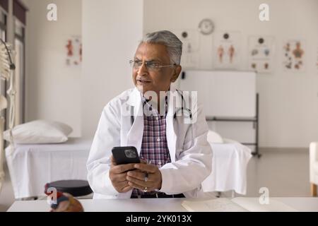 Pensive male doctor using modern smartphone in clinic office Stock Photo