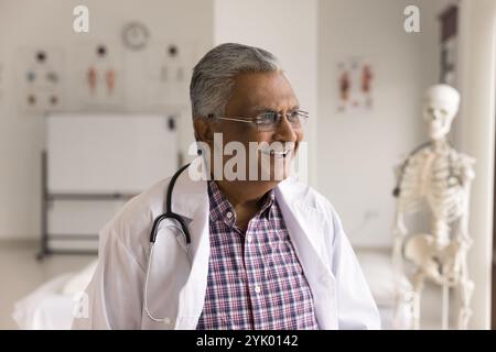 Older man doctor smiling looking aside standing in medical office Stock Photo