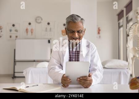 Senior 65s doctor using digital tablet at workplace clinic office Stock Photo