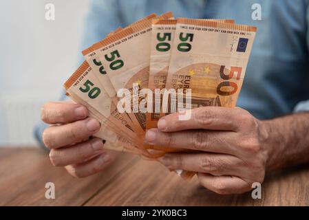 Person fanning out multiple 50 euro banknotes on a wooden table. Concept of wealth, financial security, and savings. Stock Photo