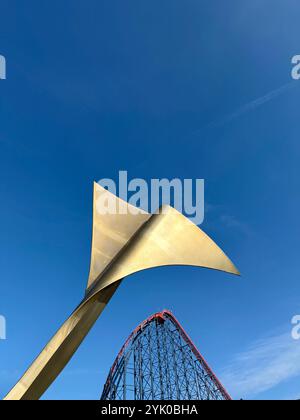 Abstract fin (Whale's Tail) on bench on Blackpool South promenade with the Big One rollercoaster ride in background against a blue sky. Blackpool, UK Stock Photo