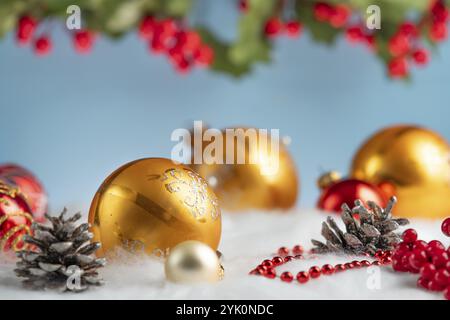Golden and red Christmas baubles lie on artificial snow, surrounded by cones and red berries Stock Photo
