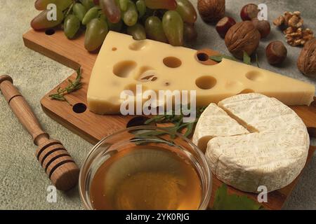 Cheese with big holes, emmental, maasdam, brie cheese, on a cutting board, with grapes and honey, nuts, appetizer to wine, top view Stock Photo