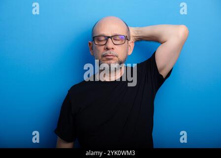 Bearded, bald man wearing glasses and a black shirt with one arm on his head. Confident and focused. Studio shot. Stock Photo