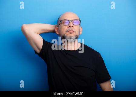 Bearded, bald man wearing glasses and a black shirt with one arm on his head. Confident and focused. Studio shot. Stock Photo