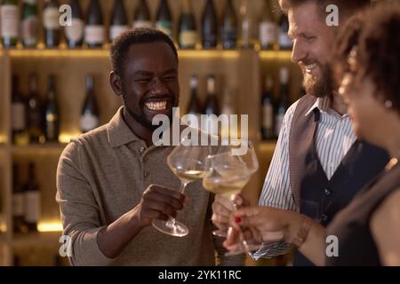 African American sommelier smiling widely while clinking glasses with his biracial colleagues and celebrating successful degustation Stock Photo