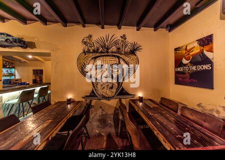 A mural inside MosaCaña Bar & Kitchen, Penstraat 41, Willemstad, depicts an elderly man wearing a sombrero, with an agave motif – a nod to tequila tradition. Next to it hangs a Don Julio advertising poster bearing the slogan "A Nod to the Dons". Don Julio González founded his tequila brand in 1942 in the Mexican state of Jalisco. Stock Photo