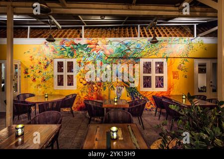The interior of MosaCaña Bar & Kitchen, Penstraat 41, Willemstad, Curaçao: Francis Sling’s mural featuring a peacock and tropical fruits dominates the yellow back wall of the semi-open dining area. The interior of the old colonial building with its terracotta-tiled roof combines rustic wooden furniture with a street art aesthetic; the bar serves exclusively rum, tequila and mezcal Stock Photo