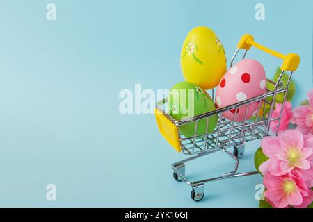Colorful painted Easter eggs in shopping cart on blue background. Sale. Shopping. Copy space Stock Photo