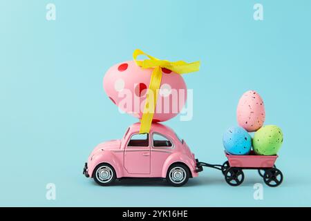 Pink car and trailer delivers eggs on blue background. Concept logistic. Shopping. Sale. Holiday preparation Happy Easter. Copy space Stock Photo