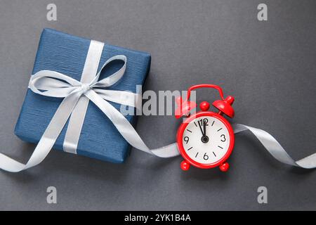 Red Alarm Clock, Dark Blue Gift box on grey background. Gift of Time. Gift for men. Fathers day. Present for him. Stock Photo