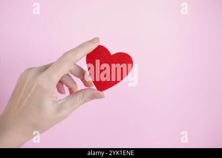 female hand holding a red heart. The concept of sincere devotion to faith. Donation, life saving or charity concept. Close-up Stock Photo
