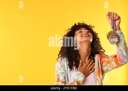 Happy winner showing different medals on yellow background. Space for text Stock Photo