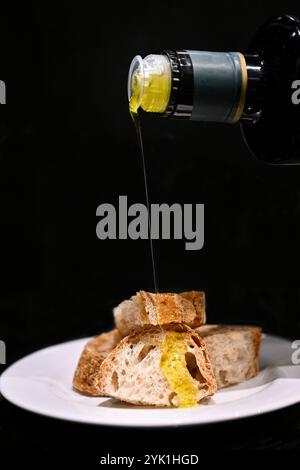 a drizzle of Italian extra virgin olive oil poured on warm wood-fire bread on black background Stock Photo