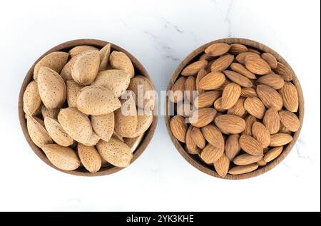 Wooden bowl with shelled almonds and peeled almond kernels on a white background. Top view, macro. Stock Photo