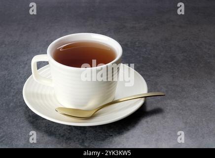 A cup of tea in a white ceramic mug and a spoon on a gray background. Stock Photo