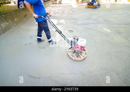 Worker using self-leveling power trowel machine with gas engine has wheels with pads, plate and he is driving it in circles smoothing surface on concr Stock Photo