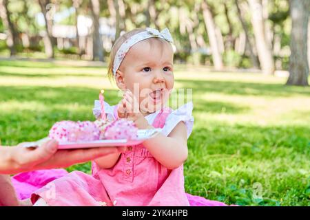 Baby girl in a pink dress clapping with excitement while celebrating her birthday with pink cake pops in a park. Stock Photo