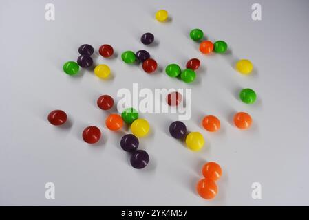 Beautiful, bright chewing and chocolate candies covered with sugar-colored enamel are located on a white plastic background. Stock Photo