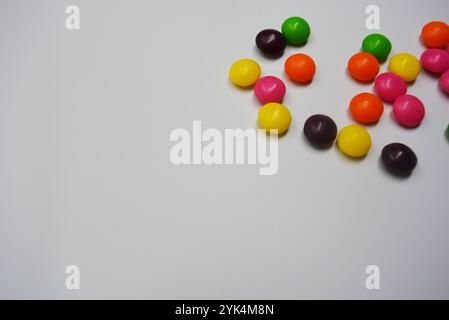 Beautiful, bright chewing and chocolate candies covered with sugar-colored enamel are located on a white plastic background. Stock Photo