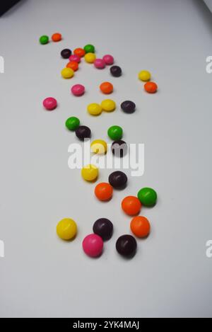 Beautiful, bright chewing and chocolate candies covered with sugar-colored enamel are located on a white plastic background. Stock Photo
