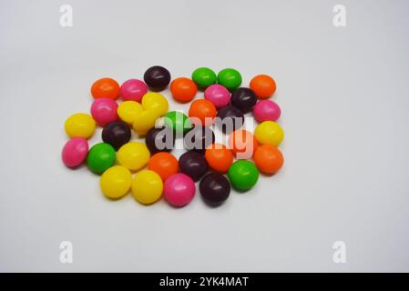 Beautiful, bright chewing and chocolate candies covered with sugar-colored enamel are located on a white plastic background. Stock Photo