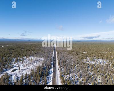 High angle aerial view of a straight asphalt highway cutting through a snow-dusted pine forest under a clear blue sky in southern Oregon Stock Photo