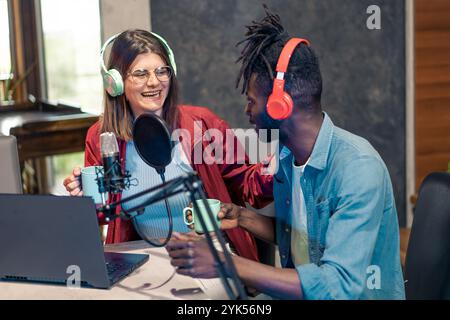Diverse young podcast hosts laughing while recording audio content in modern home studio with professional equipment Stock Photo