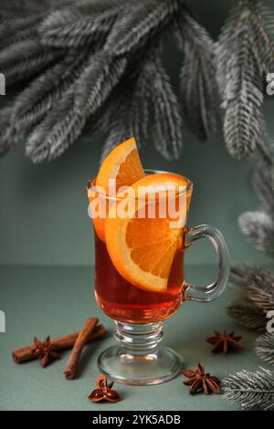 Mulled wine in glass glasses decorated with cinnamon sticks on green background, nearby are green spruce branches. Christmas drink, New Year's punch. Stock Photo