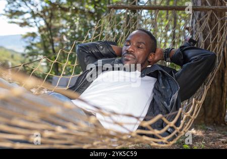 Carefree African American man enjoying a glamping getaway from the urban city, smiling wide while relaxing in a hammock. Stock Photo