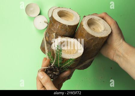 DIY Christmas candle holder made of pine logs, candles, craft rope, fir branches and cones. Hands attach the decoration. Step-by-step instructions fla Stock Photo