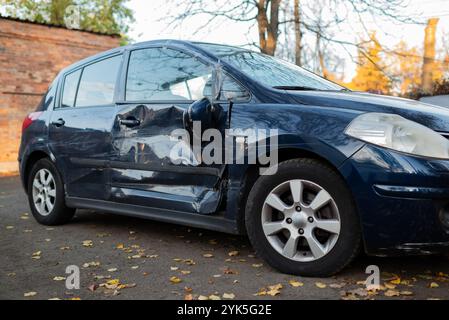 Damaged blue car with dents and scratches on the side, showing the aftermath of an accident or collision in an urban outdoor setting. Stock Photo