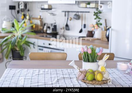 Easter decoration of colorful eggs in a basket and a rabbit on the kitchen table in a rustic style. Festive interior of a country house Stock Photo