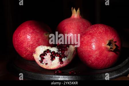 Close-up of ripe red pomegranates lying on an old metal tray. A pomegranate is cut open. Stock Photo
