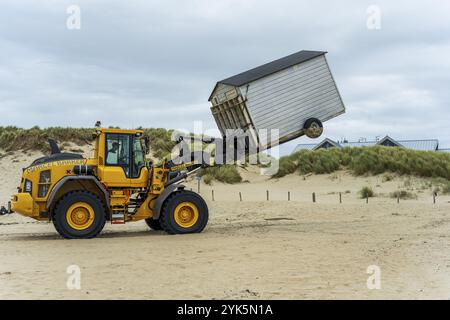 A yellow tractor lifts a beach cabin near the dunes of a sandy beach, end of season on Texel Stock Photo