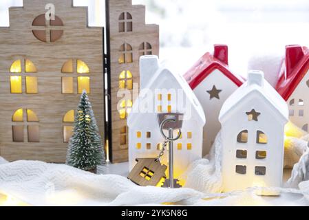 Key and tiny house of a small size on cozy home with Christmas decor on window sill. Gift for New Year. Insurance, moving to new house, mortgage, rent Stock Photo