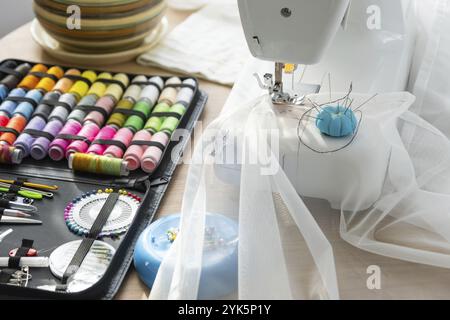 Sewing layout with multicolored spools of thread close-up, needles, electric sewing machine. Filling the thread into the sewing needle, adjusting the Stock Photo