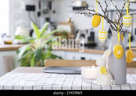 Easter decoration of colorful eggs in a basket and a rabbit on the kitchen table in a rustic style. Festive interior of a country house Stock Photo