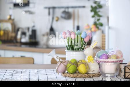 Easter decoration of colorful eggs in a basket and a rabbit on the kitchen table in a rustic style. Festive interior of a country house Stock Photo