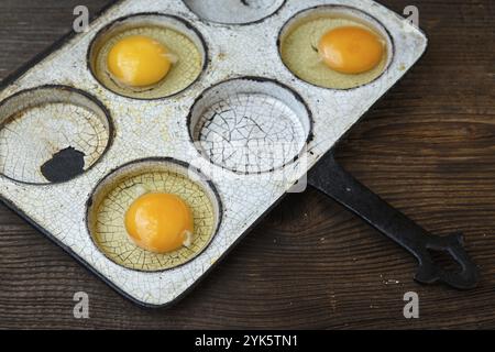 Eggs in old heavy duty steel frying pan isolated on wooden background Stock Photo