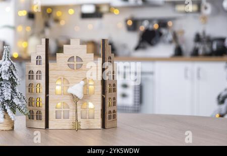 Key and tiny house of a small size on cozy home with Christmas decor on table of festive white kitchen. Gift for New Year. Insurance, moving to new ho Stock Photo