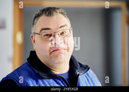 Man tries to hold back smile, face of an obese male with glasses is close-up. Stock Photo
