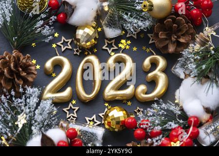 The golden figures 2023 made of candles on a black stone slate background are decorated with a festive decor of stars, sequins, fir branches, balls an Stock Photo